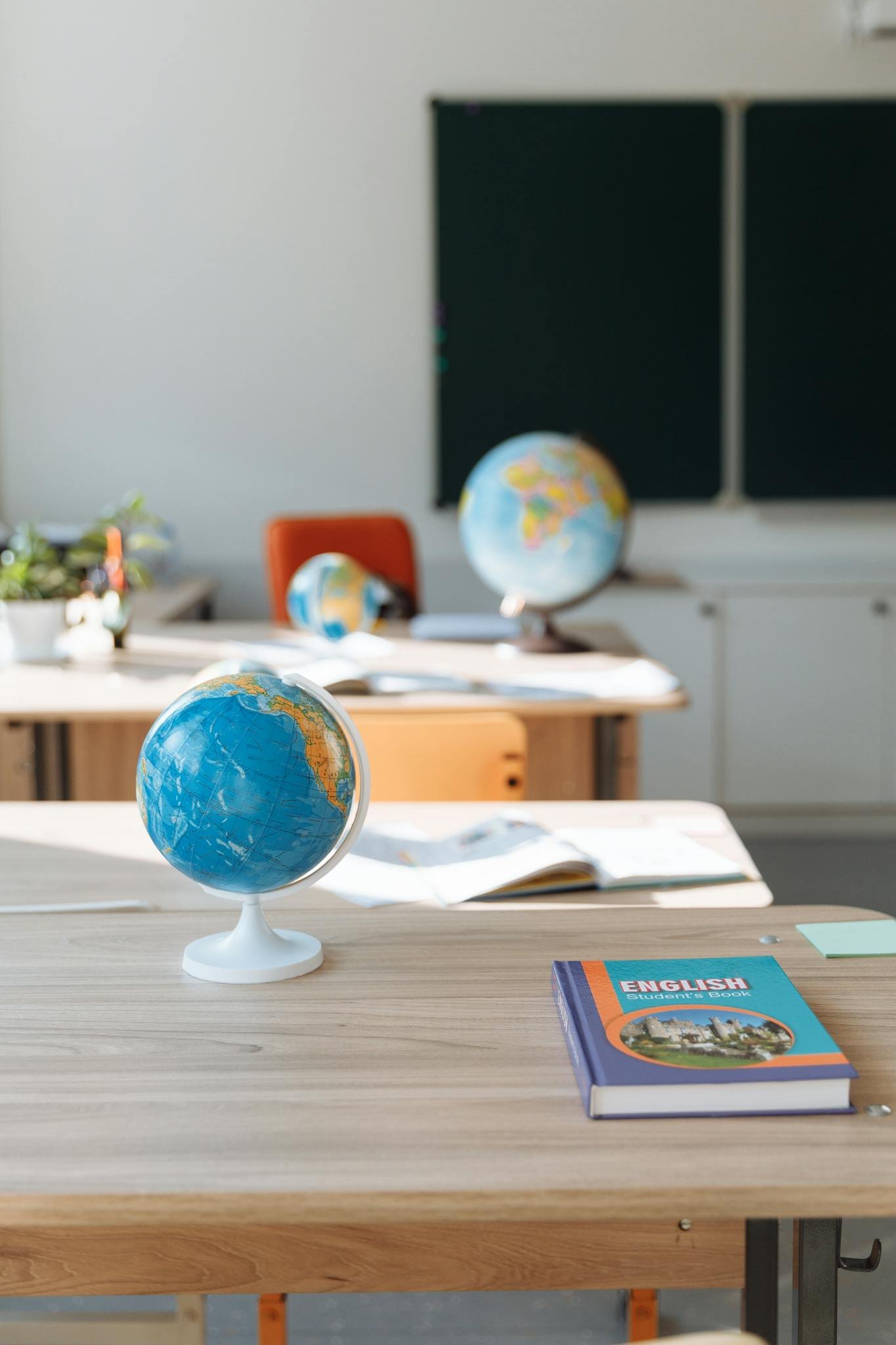 Classroom interior featuring globes, English book, and desks in sunlight